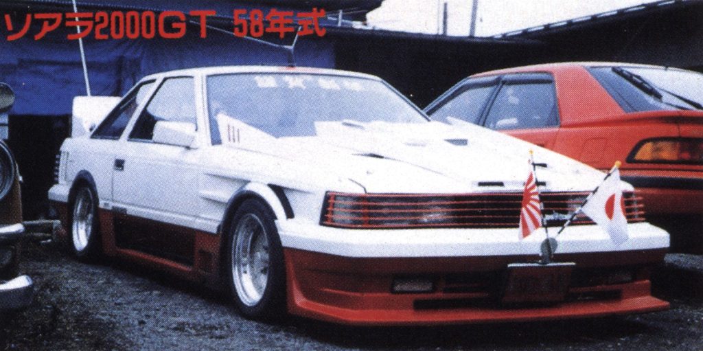 Modified Toyota Soarer 2000GT from 1983 (Showa 58), featuring flags, parked next to another car in a lot.