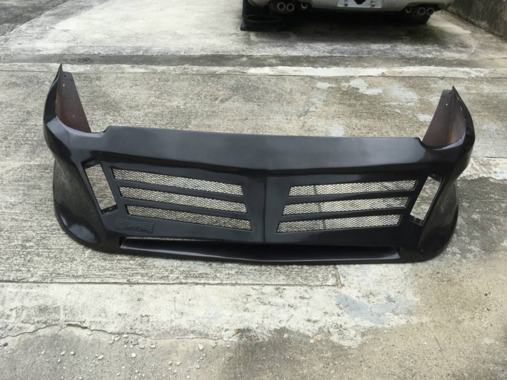Black aftermarket car bumper with mesh grills on concrete floor, showcasing the brand Auto Craft in Japanese kanji.
