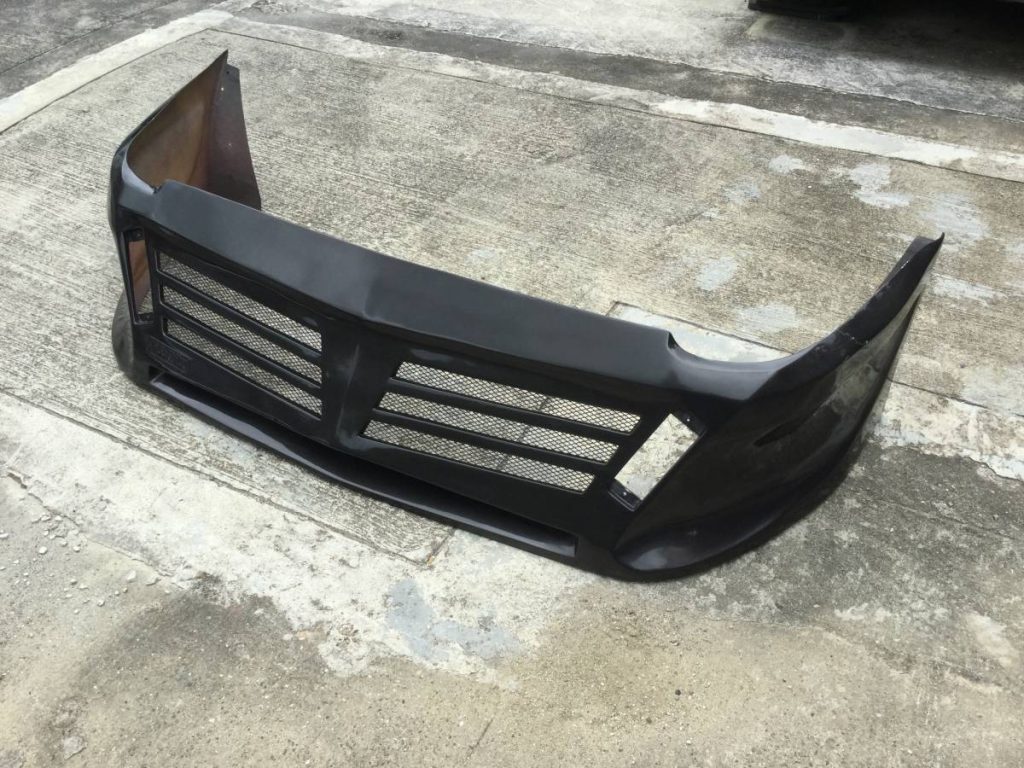 Front bumper of a car, black with grill design, placed on a concrete surface