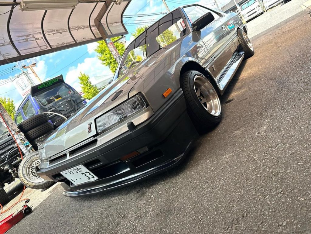 A classic JDM sports car at a Japanese auto shop, with a license plate displaying the number 33.