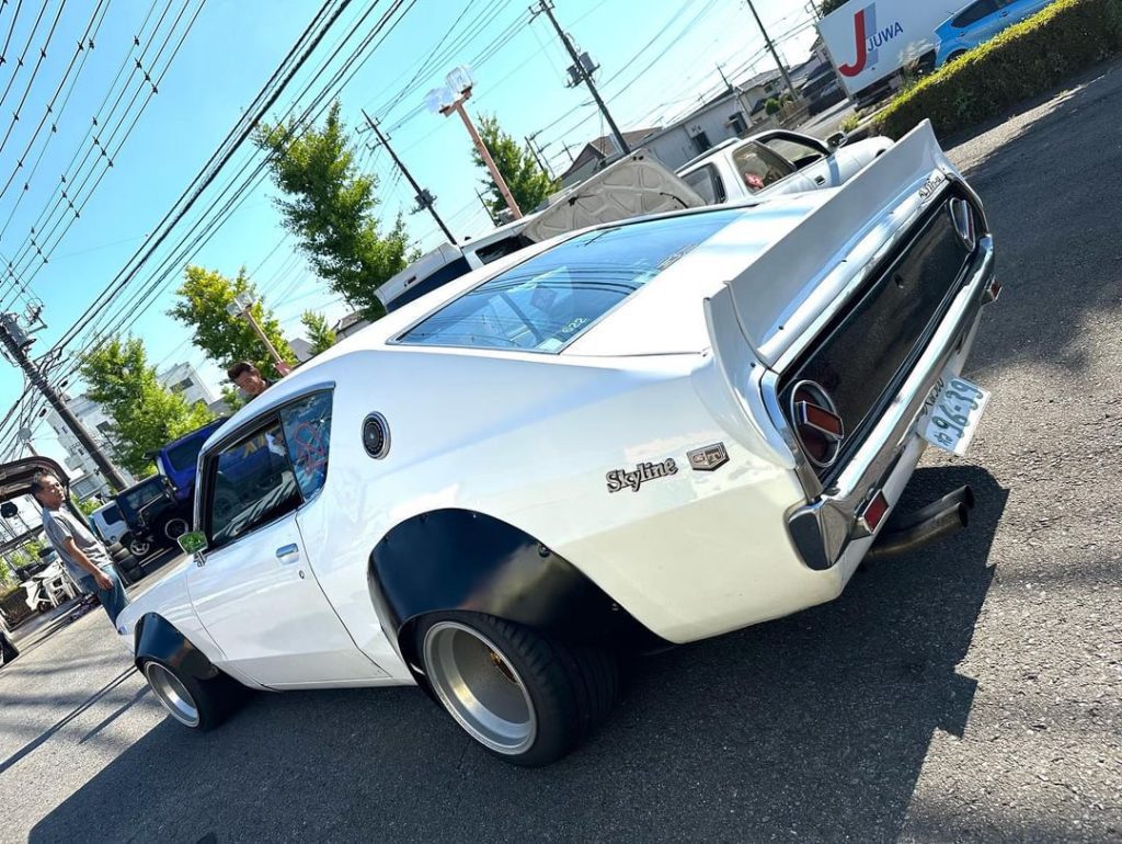 Vintage white Nissan Skyline GT-R parked on a sunny street in Japan, showcasing its classic body style.