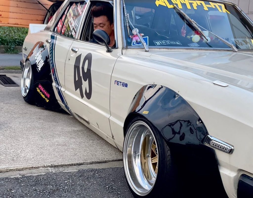 Custom white Japanese car with number 49, wide fenders, and stickers, parked on a street.