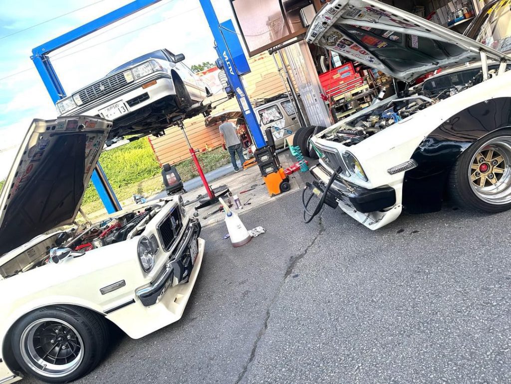 Classic cars under maintenance at an auto repair shop. Mechanics working with hoods up and vehicles lifted.