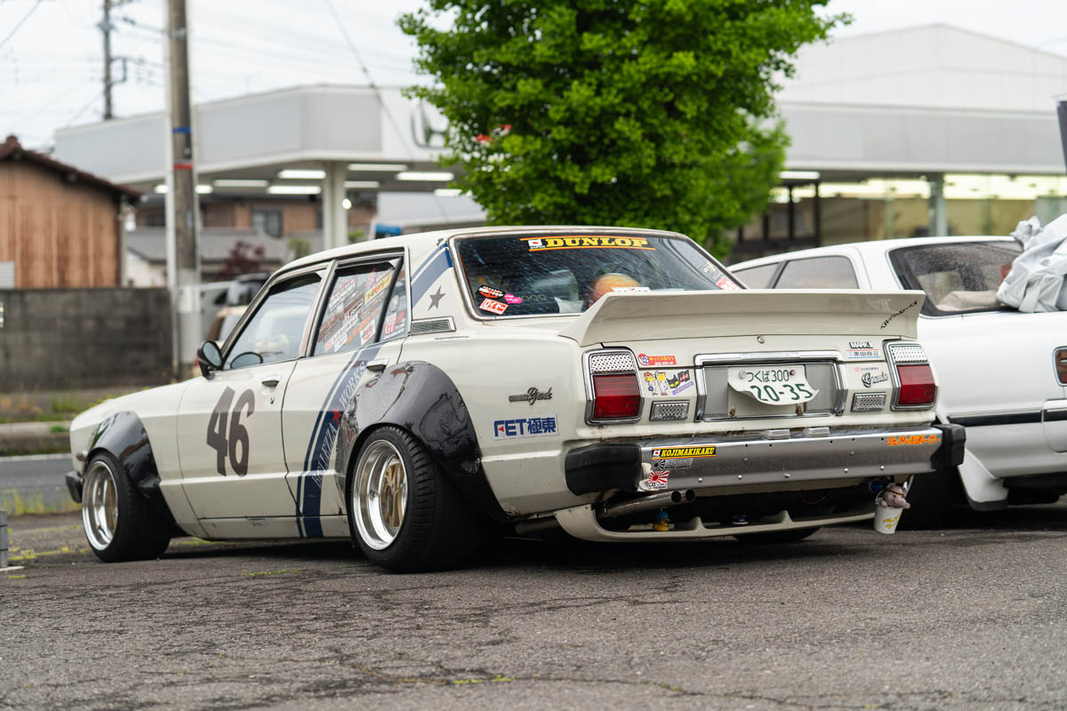 Modified vintage car with number 46, adorned with various stickers including Dunlop, parked near an urban gas station.