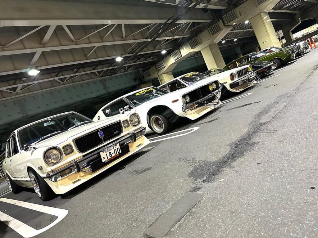Lineup of vintage Japanese cars under bridge, showcasing classic retro design and tuning culture.