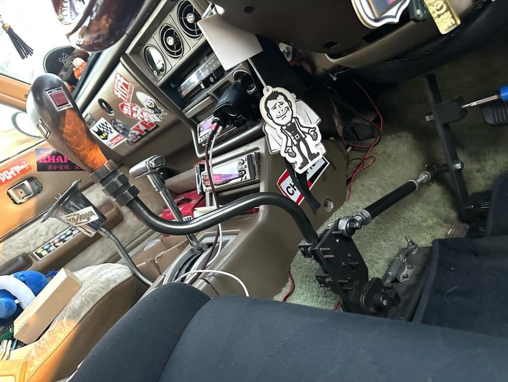 Vintage car interior with Japanese decorations, gear shifter, and a character keychain in the front seat.