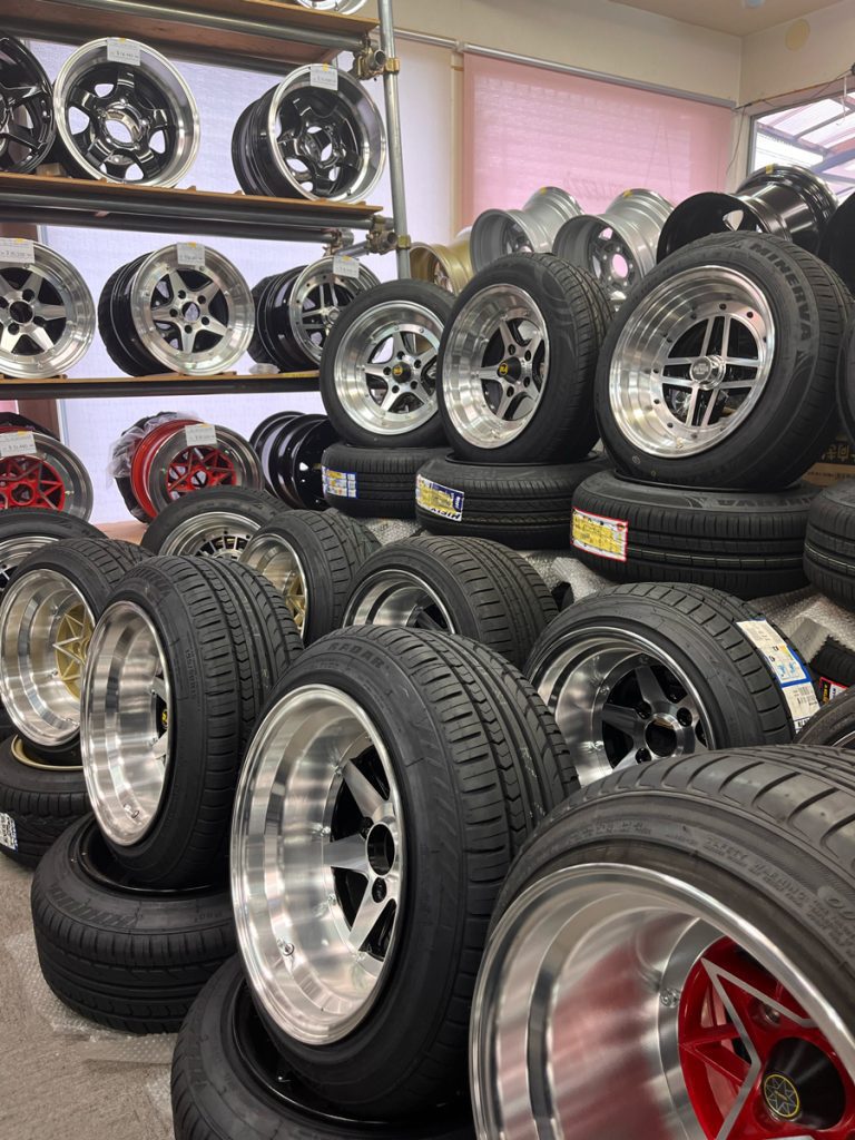Display of various alloy car wheels and tires in a Japanese auto shop. High-quality rims and tires for sale.