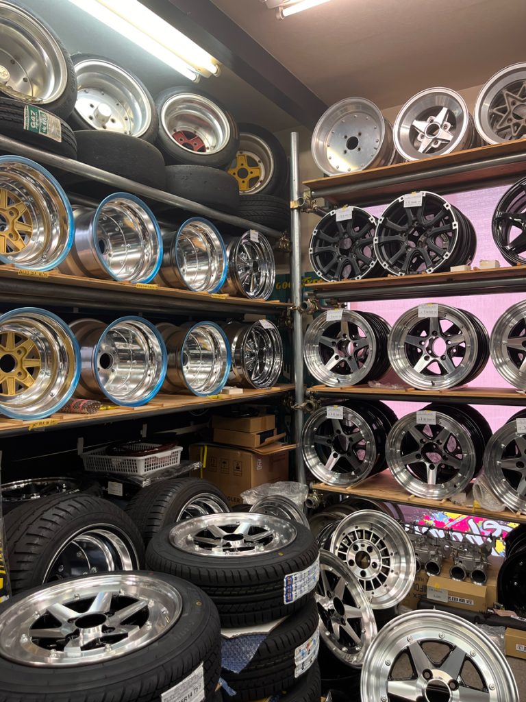Alt text: Collection of assorted alloy wheels and tires on shelves in a car accessories shop in Japan.