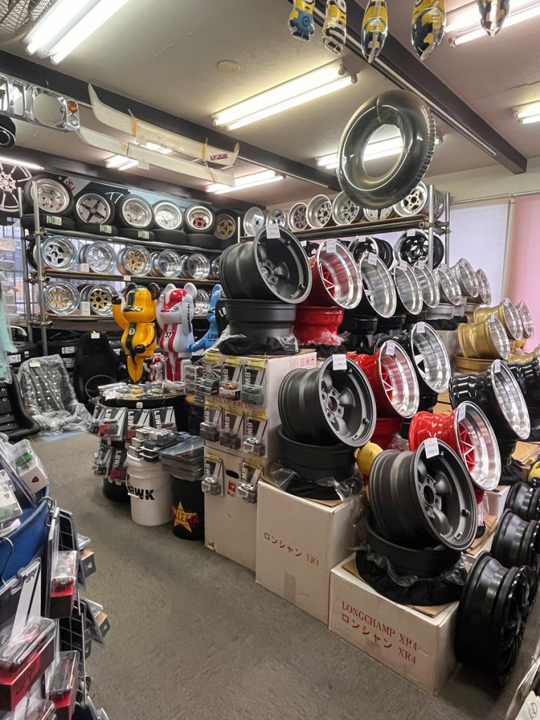 Auto parts shop with a wide selection of wheels and rims, featuring Longchamp XR4 branded boxes and colorful displays.