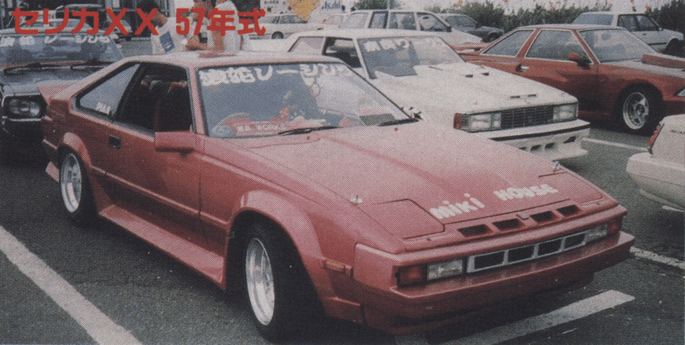 Vintage 1982 Toyota Celica XX with custom modifications at a car meet, featuring Japanese text on the windshield.