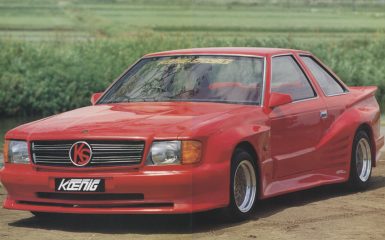 Red Koenig Specials car with sporty design and wide body kit, parked outdoor near a green field.