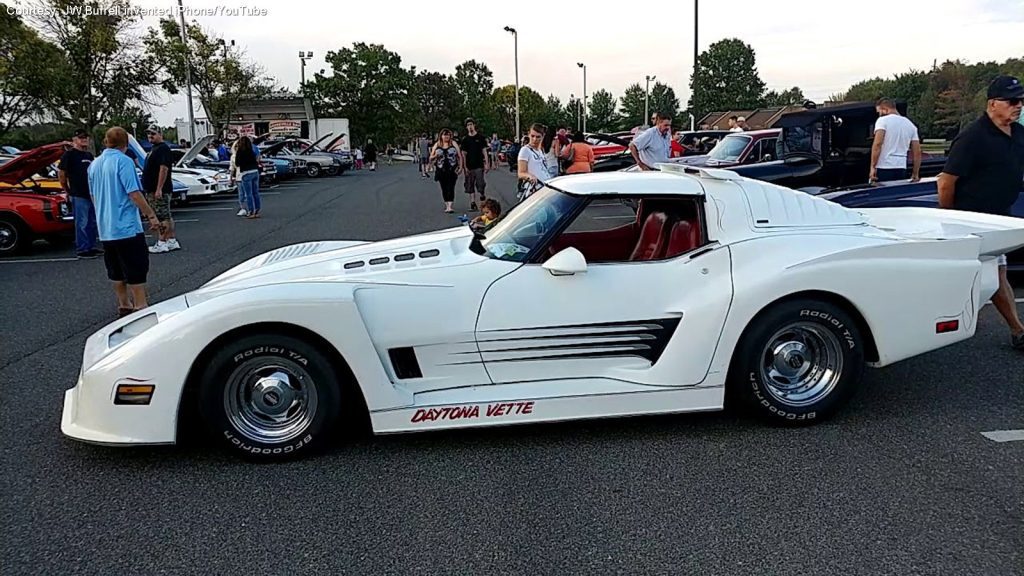 Classic white Daytona Vette at a car show with people admiring various vintage cars in the background.