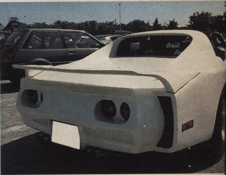 Custom white sports car with a unique rear design, parked in a lot with other vehicles.