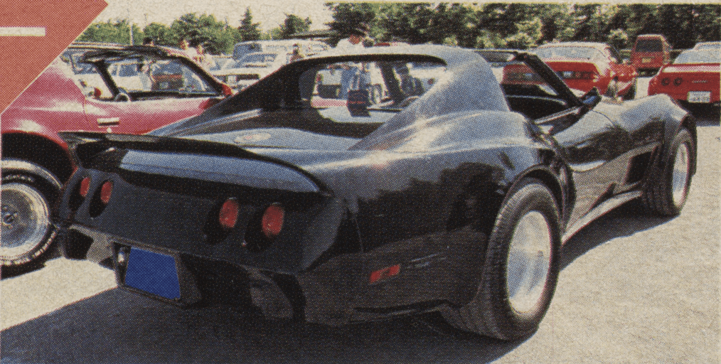 A classic black sports car with targa top parked at an outdoor car show, surrounded by other vintage cars.