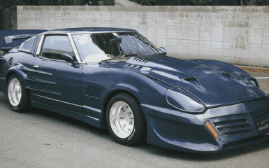 Modified blue Nissan 280ZX sports car with wide fenders, large rear wing, and custom body kit parked near concrete wall.