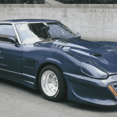 Modified blue Nissan 280ZX sports car with wide fenders, large rear wing, and custom body kit parked near concrete wall.