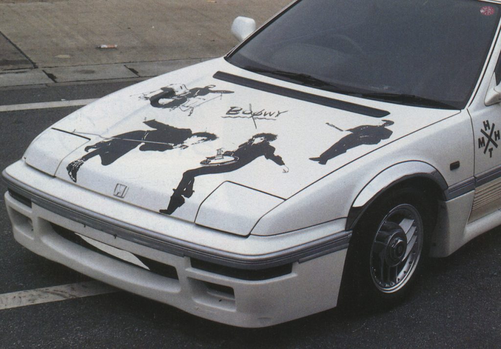 White Honda car with Boøwy band graphics on hood, Japanese text H X T on side; street view.