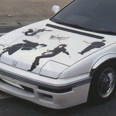 White Honda car with Boøwy band graphics on hood, Japanese text H X T on side; street view.