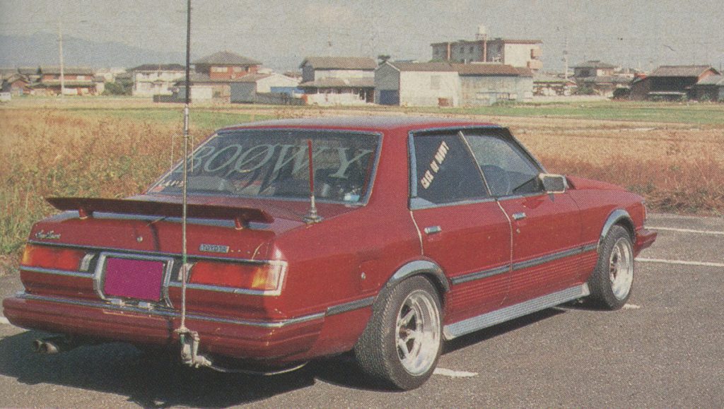 Vintage red Japanese car with rear spoiler and custom decals parked in rural area