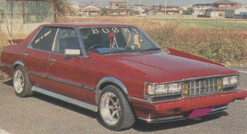 Vintage red car from 1980s Japan with BOOWY decal on windshield and a sticker on the side window.