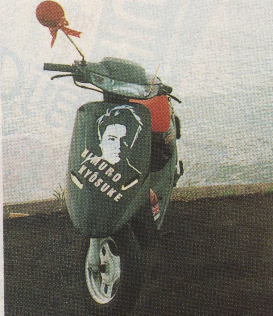 A Honda Dio AF18 scooter with a portrait and the text HIMURO KYOSUKE parked by a lake shore.