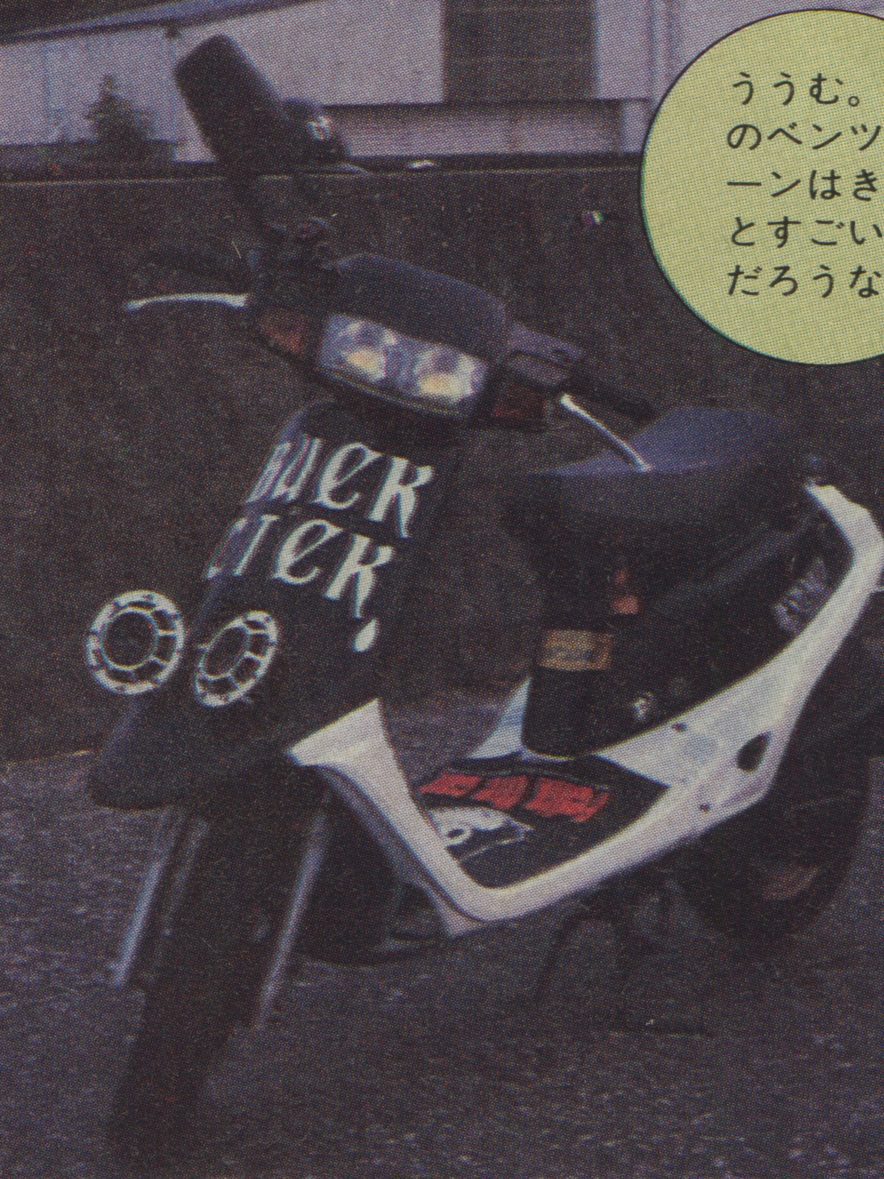 Black and white scooter with custom Black Rider text and speakers on front, parked outdoors with Japanese text.