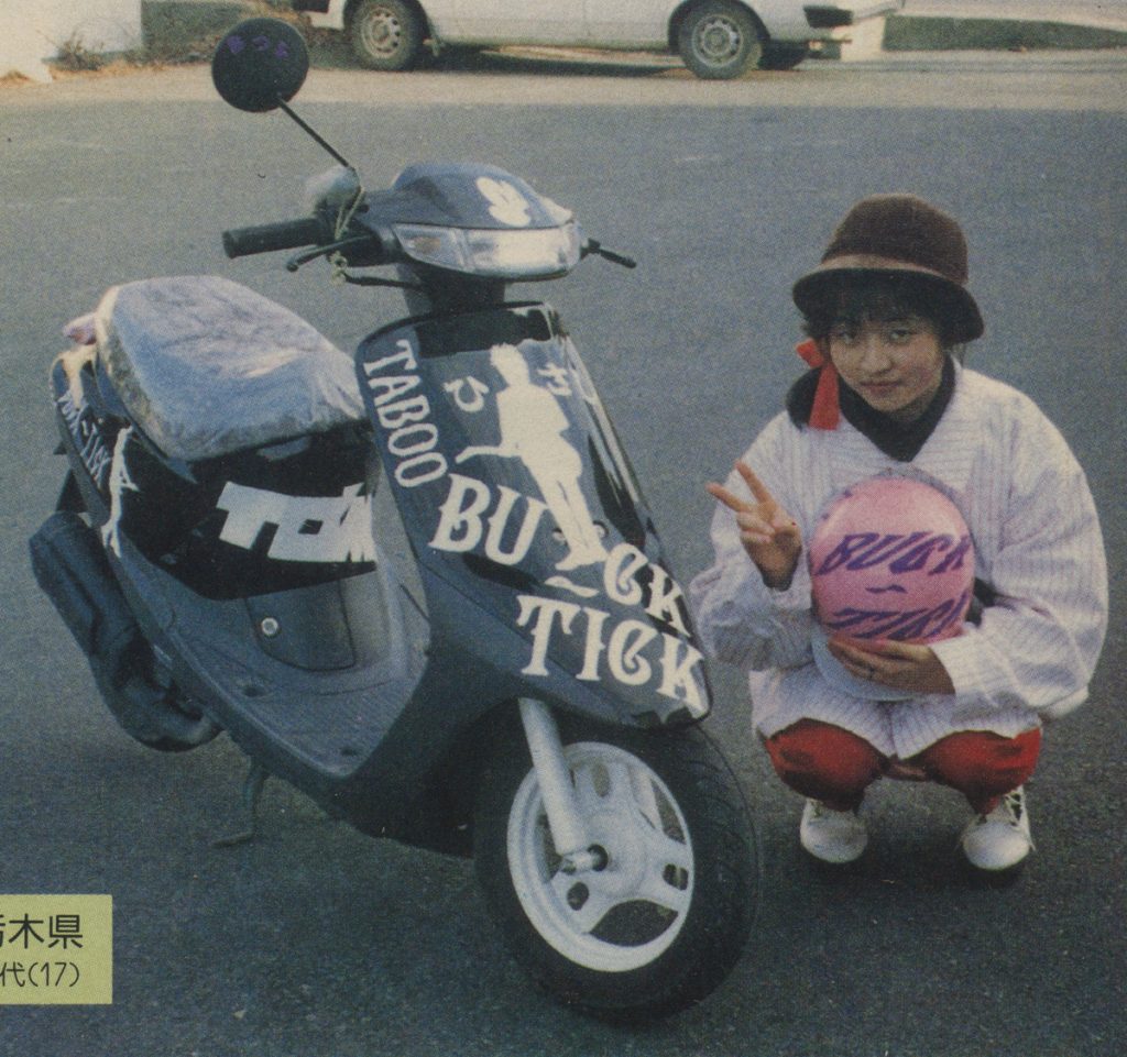 Teen girl posing with decorated scooter and 'Buck-Tick' helmet, making peace sign; Japanese characters indicate 'Tochigi Prefecture.'