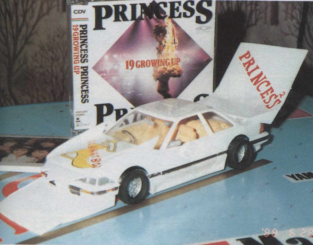 Model toy car next to Princess Princess 1990 Growing Up album on table, creating a nostalgic scene from the '90s.