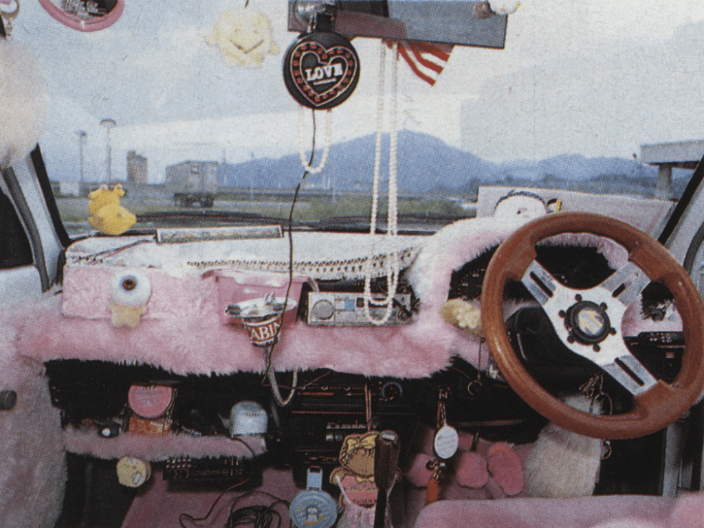 Heavily accessorized car interior with pink fur, a wooden steering wheel, and various plush toys and hanging decorations.