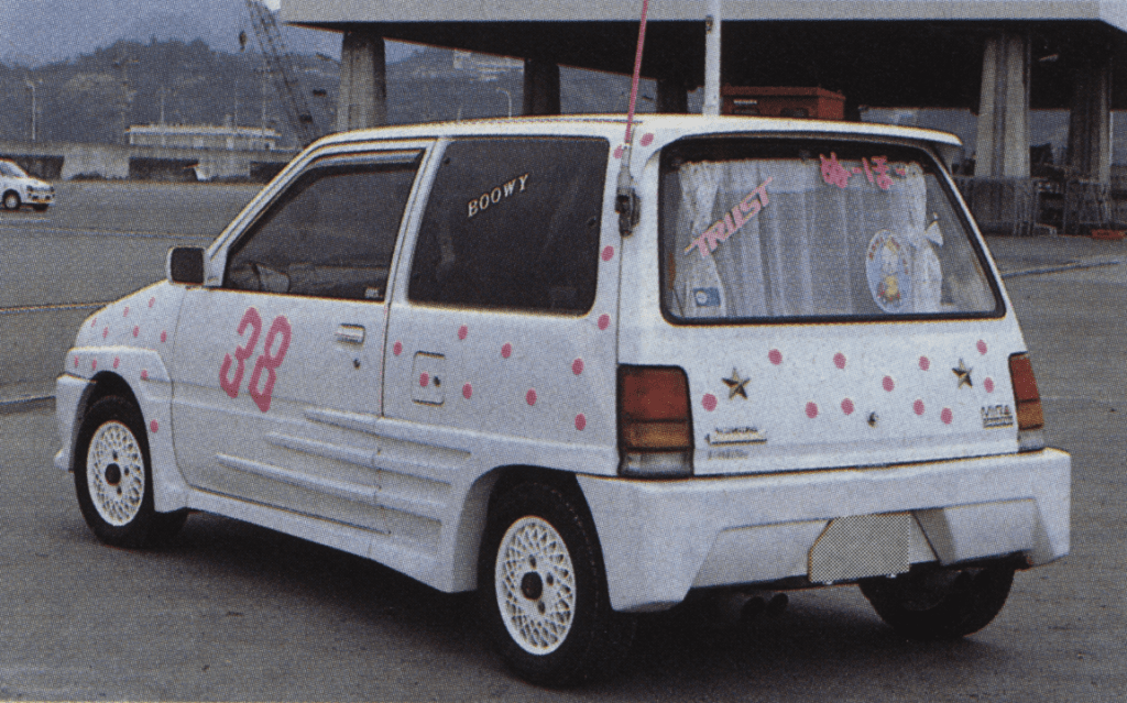 Rear view of a customized white car with pink polka dots, 38 on door, BOØWY on window, and TRUST on rear curtain.