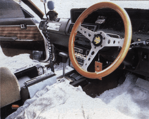 Vintage car interior with a wooden steering wheel, showy dashboard, radio equipment, and Japanese text.