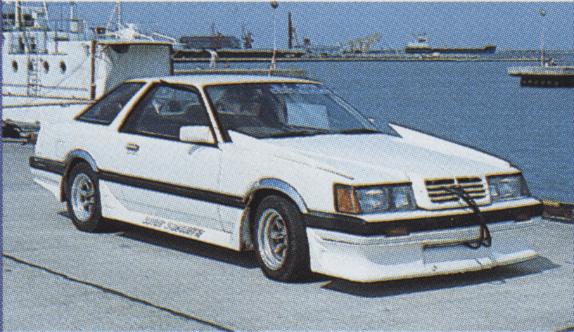 White modified Nissan F30 leopard coupe car with Blue Spirit written on the side, parked near the dock with boats and water in the background.