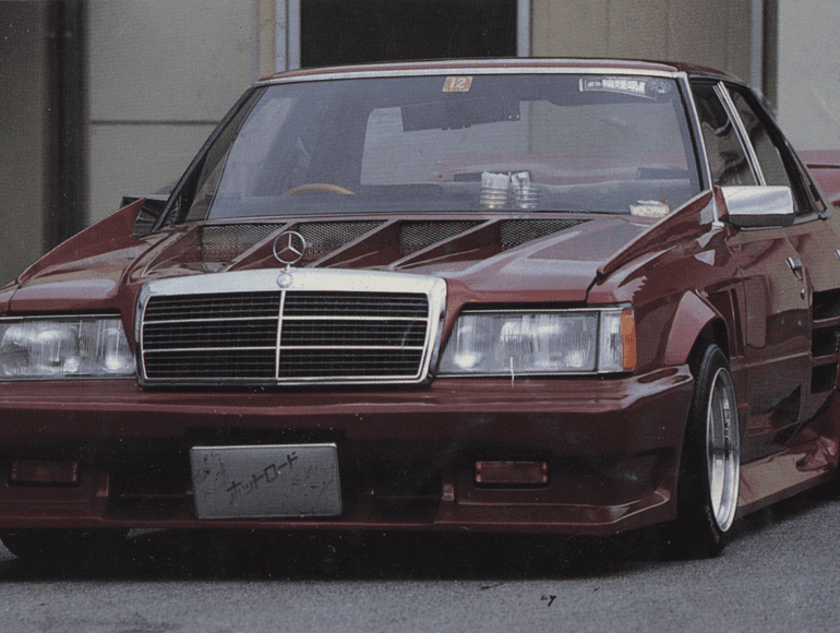 Customized vintage Mercedes-Benz with aggressive body kit and low stance; Japanese license plate reads ナツロード meaning Nat Road.