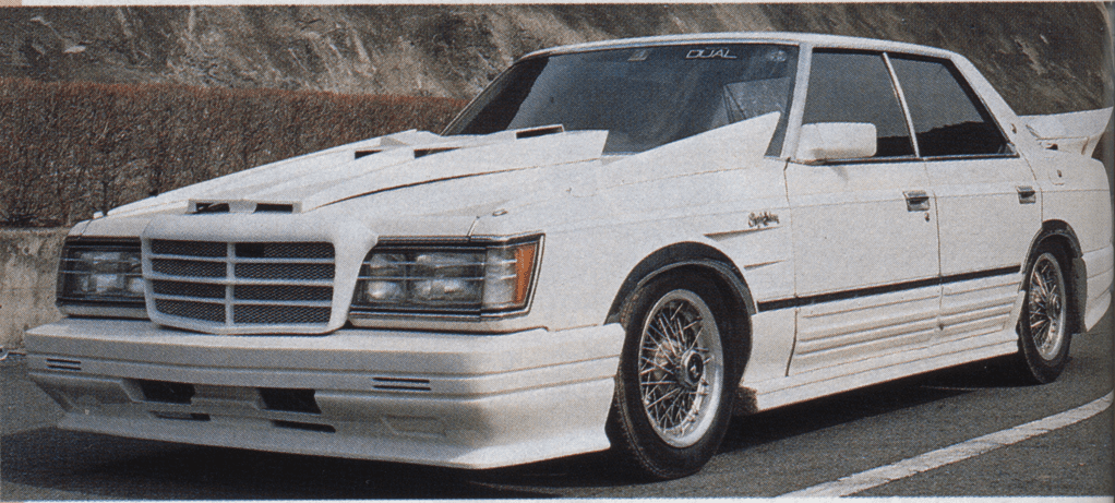 A white modified Toyota S110 Crown Japanese sedan with a custom body kit and wire spoke wheels, labeled DUAL on the windshield.