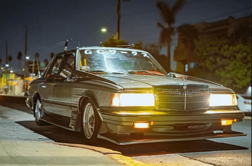 Vintage Japanese car with bright headlights and G Cワークス (G C Works) decal on the windshield, parked at night.