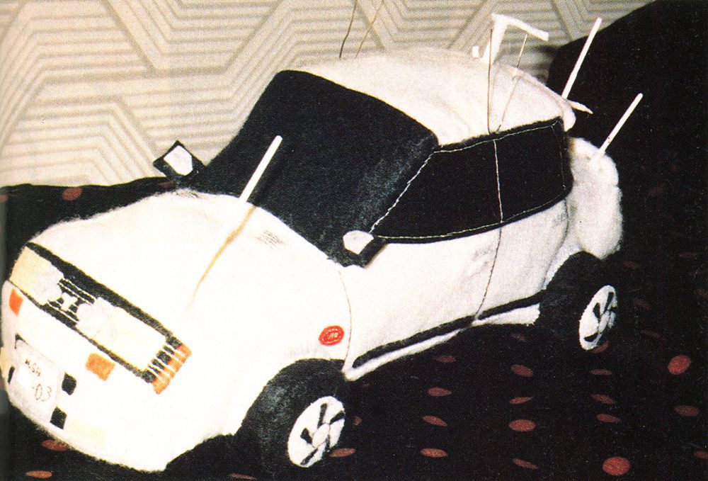 Plush toy car with antennas, white and black design, on a polka-dot surface. License plate displays Japanese text and 03.