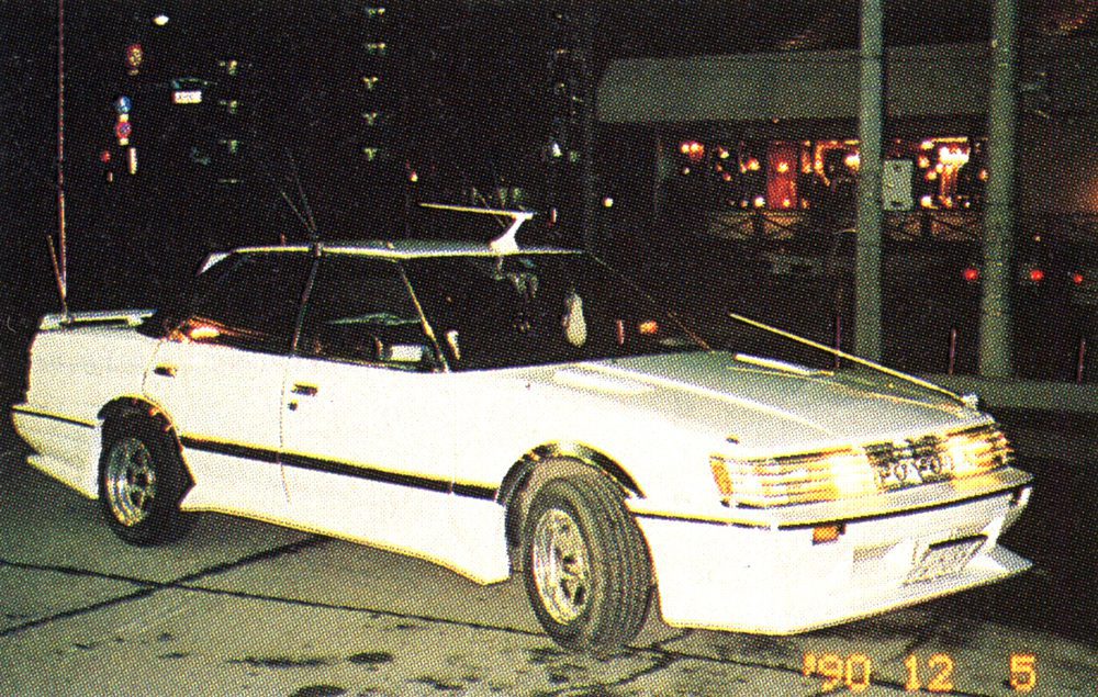 Retro white car on a city street at night, dated December 5, 1990, Japan.