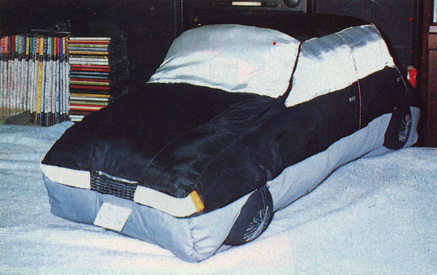 Plush car toy on bed with colorful books in background. Cozy decor.