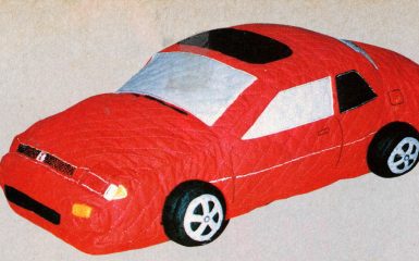 Toy red car with a quilted design, featuring realistic details on wheels and windows, on a beige background.