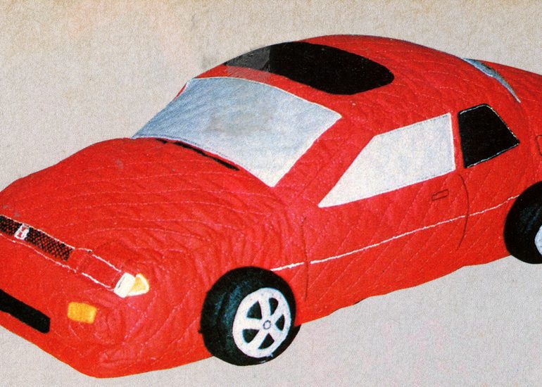 Toy red car with a quilted design, featuring realistic details on wheels and windows, on a beige background.