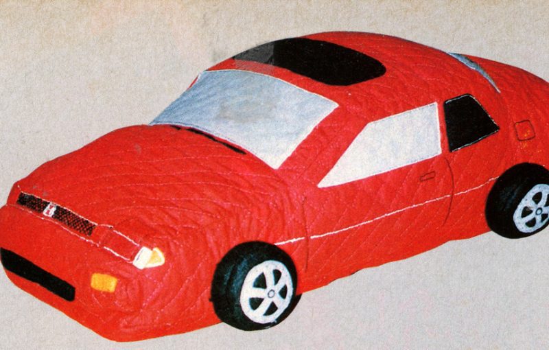 Toy red car with a quilted design, featuring realistic details on wheels and windows, on a beige background.