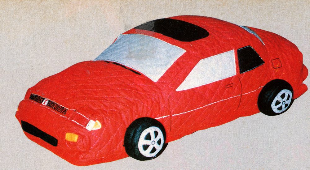 Toy red car with a quilted design, featuring realistic details on wheels and windows, on a beige background.