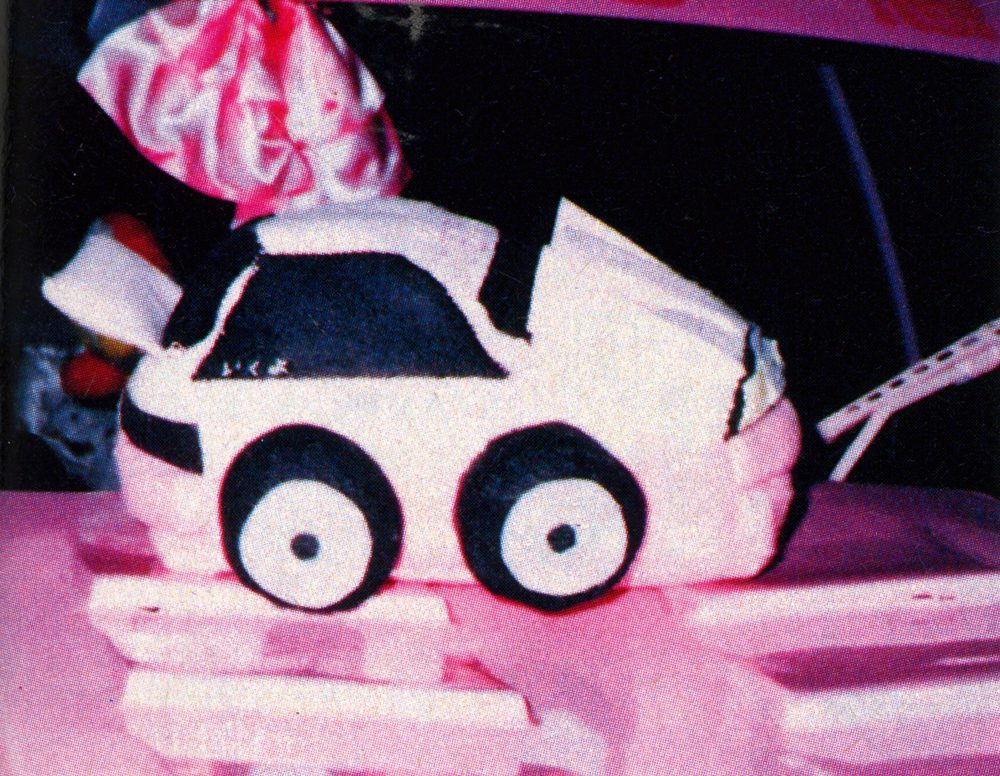 Pink and white toy car on a pink surface with a decorative pink bow.