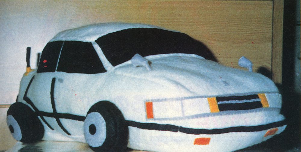 Plush toy car resembling a white police vehicle with black stripes and colorful accents.