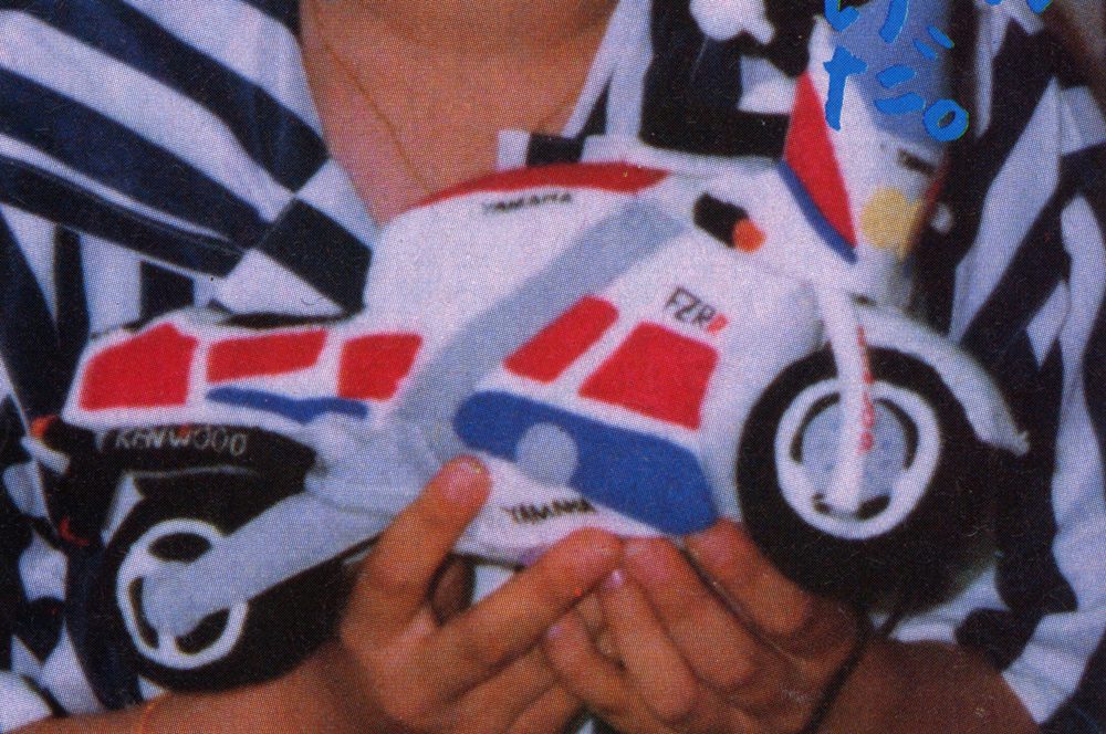 Child holding a colorful toy motorcycle with Japanese text ヤマハ (Yamaha) written on it.