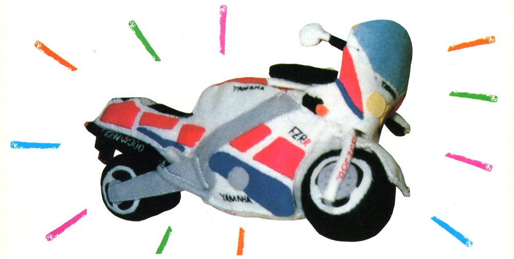 Plush Yamaha motorbike toy with colorful accents and FZR text, surrounded by colorful lines on a white background.