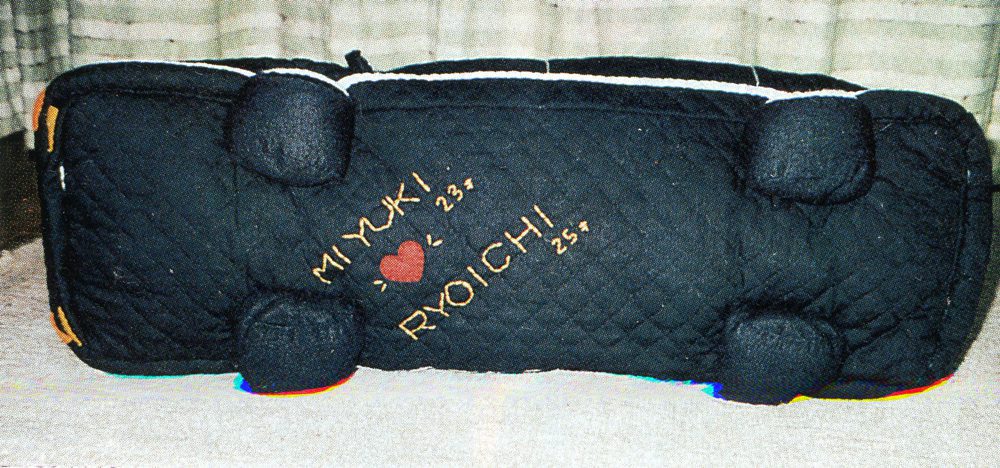 Black quilted bolster pillow with Miyuki ❤️ Ryoichi embroidered on it, showcasing a personalized design.