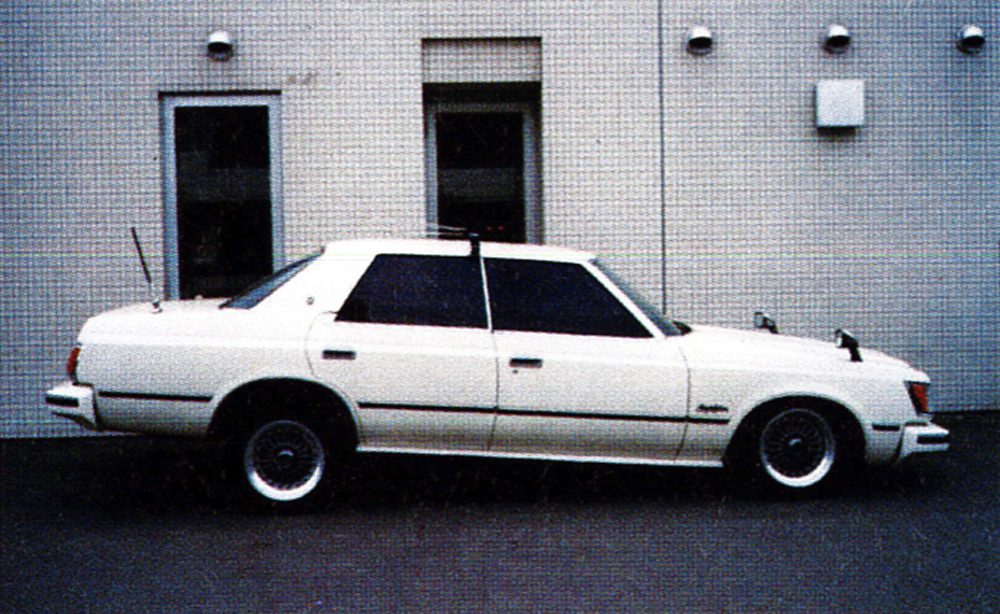 Classic white sedan parked outside a modern building, showcasing retro vehicle design.