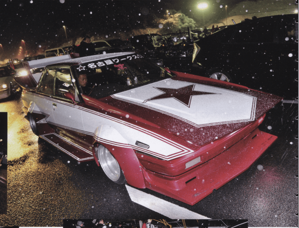 Custom bosozoku car with star decal under rain at night, surrounded by parked vehicles.