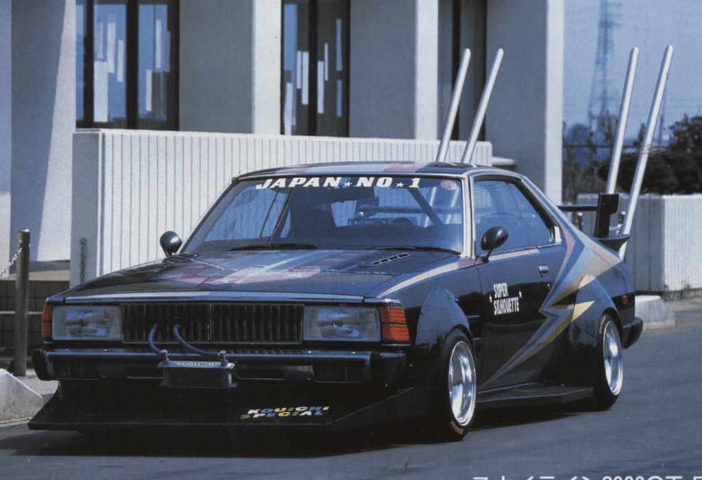 Vintage Japanese race car with bold decals and tall exhaust pipes in a modern urban setting.